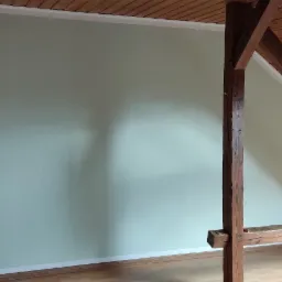 Pomalowana na jasnozielono ściana pod skosem dachu z drewnianą konstrukcją nośną, widok na fragment poddasza z drewnianą boazerią.