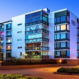 Nowoczesny budynek mieszkalny z przeszklonymi balkonami i oświetleniem zewnętrznym, widok o zmierzchu.