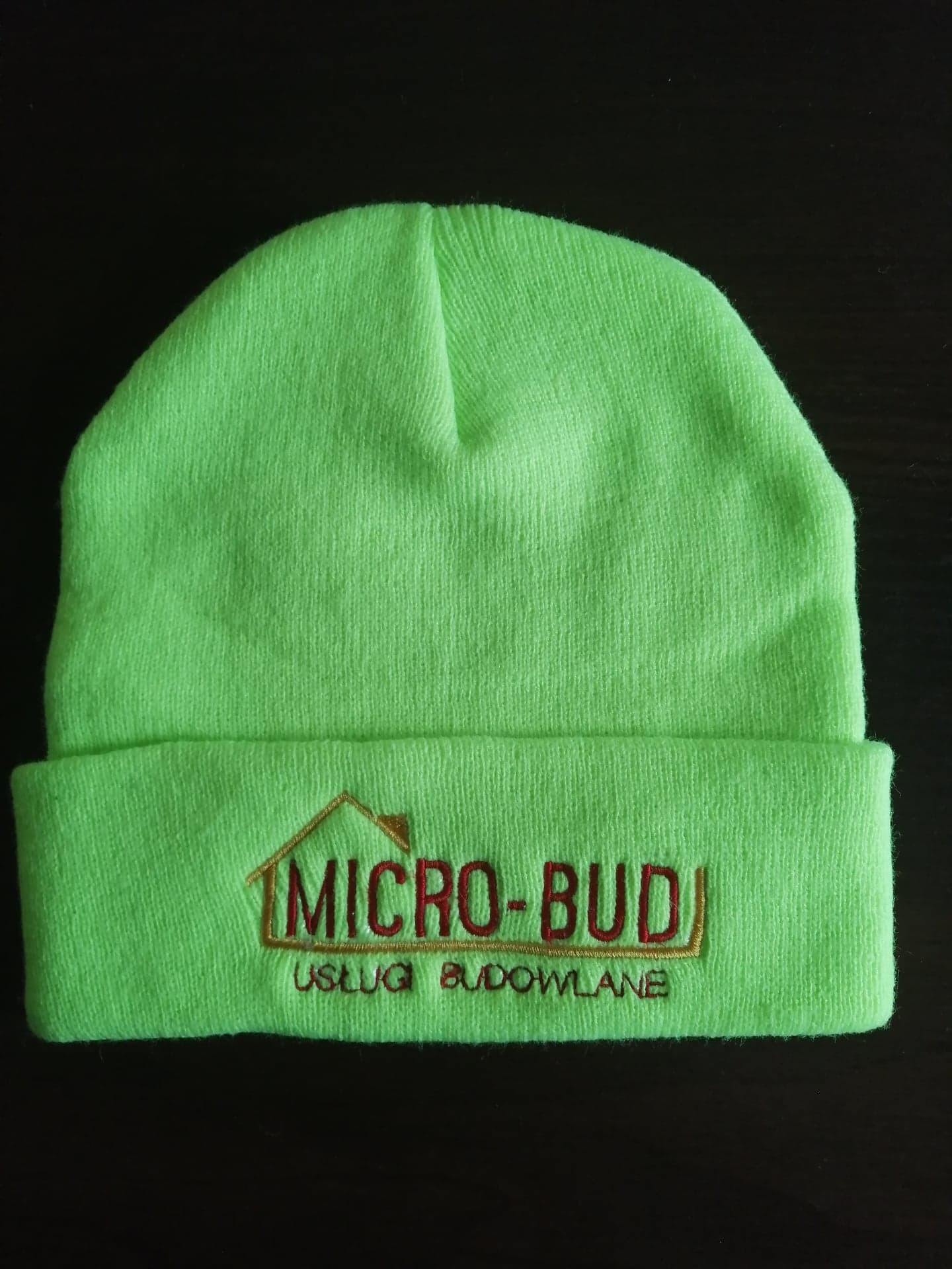 Jasnozielona czapka z wyhaftowanym logo firmy budowlanej 'MICRO-BUD' w kolorze czerwono-brązowym.