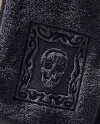 Ciemnoszary ręcznik frotte z wytłoczonym motywem czaszki w ozdobnej ramce.