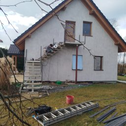 Paweł Brańka Usługi Spawalnicze - Pracownik w trakcie montażu metalowej konstrukcji schodów zewnętrznych przy ścianie budynku, widoczne narzędzia i materiały budowlane na trawie, w tle elementy ogrodu i fragment dachu