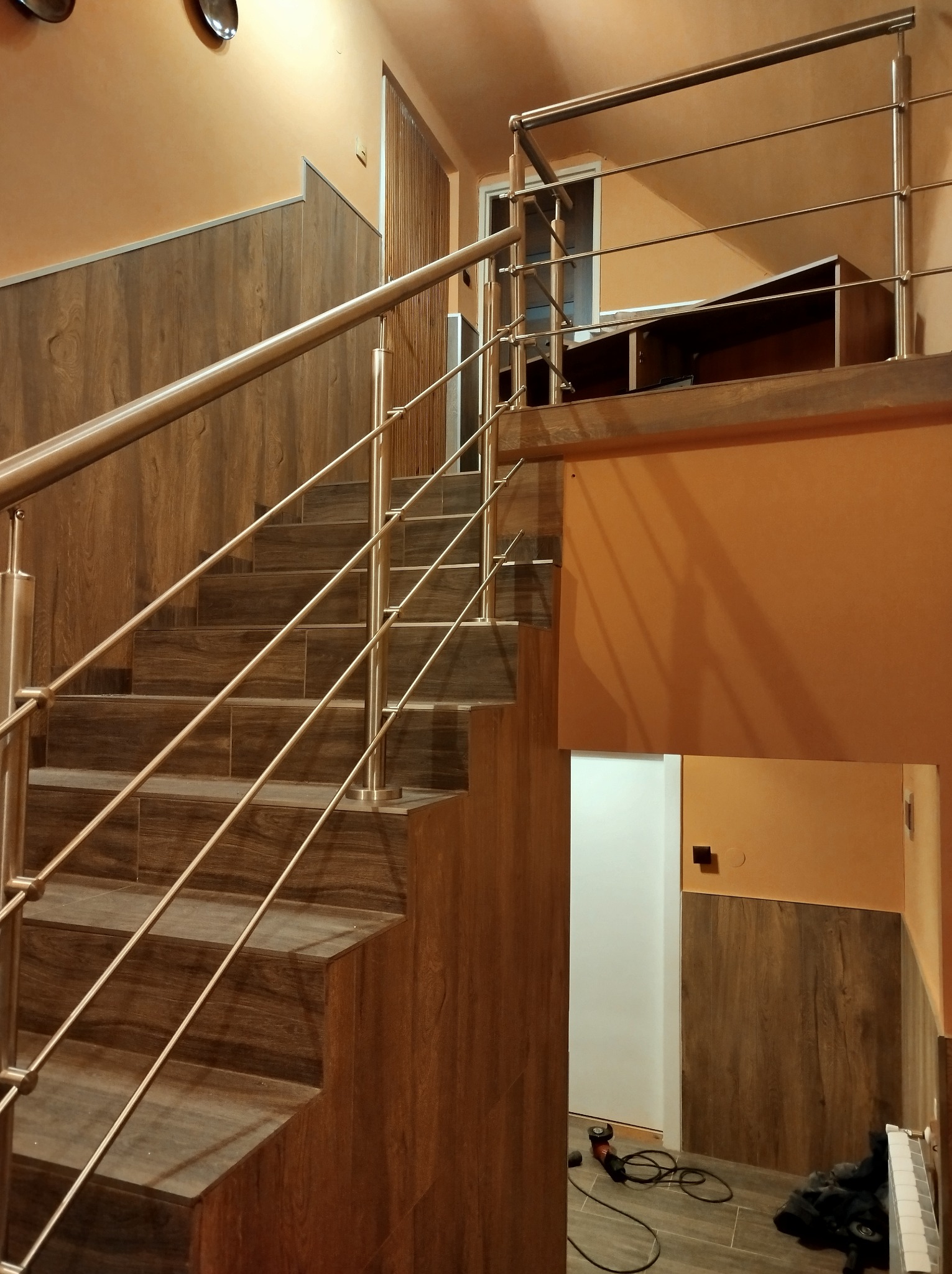 Schody wykończone drewnopodobnymi płytkami z zamontowaną balustradą ze stali nierdzewnej, widoczny fragment podłogi z narzędziami po montażu.