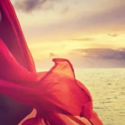 Kobieta w czerwonej, zwiewnej sukience na tle zachodzącego słońca nad morzem i okrągła reklama z tekstem 'Gorące oferty w SUPER cenie do 1500 zł!'