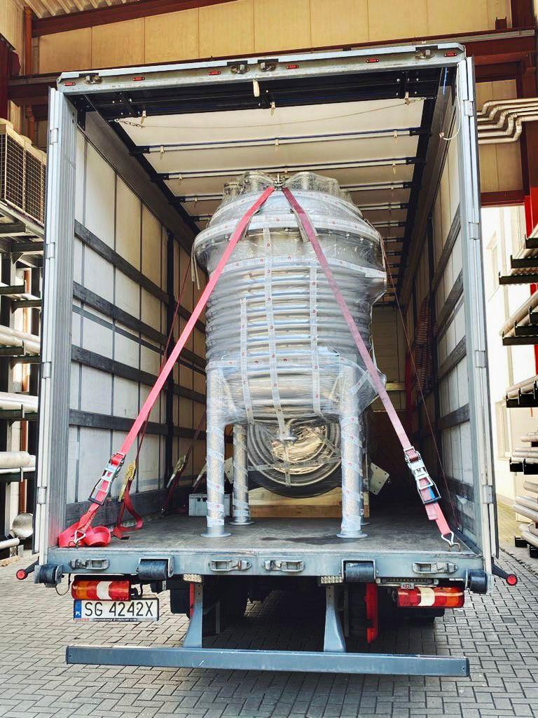 Srebrny, spiralny zbiornik przemysłowy zabezpieczony pasami wewnątrz naczepy ciężarówki z widoczną tablicą rejestracyjną SG 4242X.