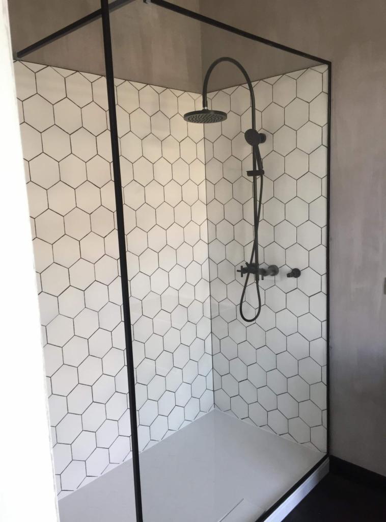 Nowoczesna kabina prysznicowa z czarną armaturą i białymi heksagonalnymi płytkami na ścianach, wykończona w minimalistycznym stylu.