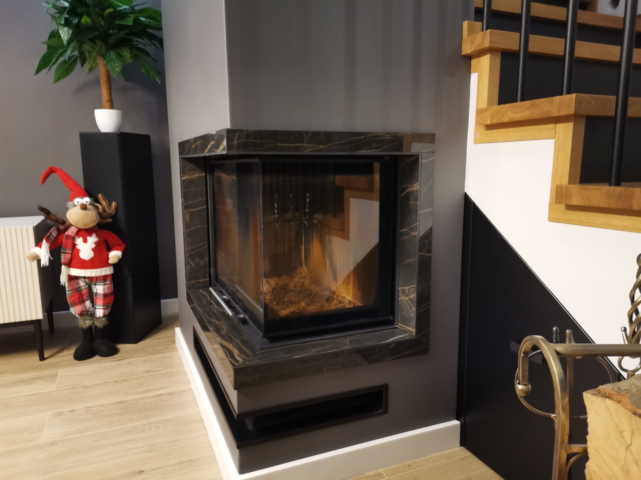 Elegancki kominek obudowany marmurem w salonie w Łabiszynie. Dekoracje świąteczne dodają wnętrzu ciepła i przytulności. Widoczne schody z drewnianymi stopniami.