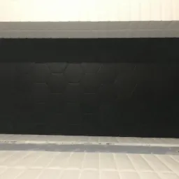 Ściana wyłożona czarnymi, heksagonalnymi płytkami ceramicznymi w górnej części i białymi, podłużnymi płytkami w dolnej części, oddzielona poziomym pasem szarego silikonu.