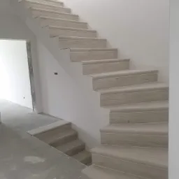 Schody wykończone panelami drewnopodobnymi w Przytkowicach, widoczne na tle surowych ścian w trakcie remontu.