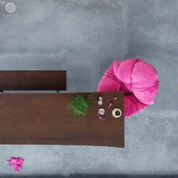 Widok z góry na stół z ciemnego drewna, różowy puf, doniczkę z trawą i akcesoria kosmetyczne na szarym tarasie graniczącym z trawnikiem.