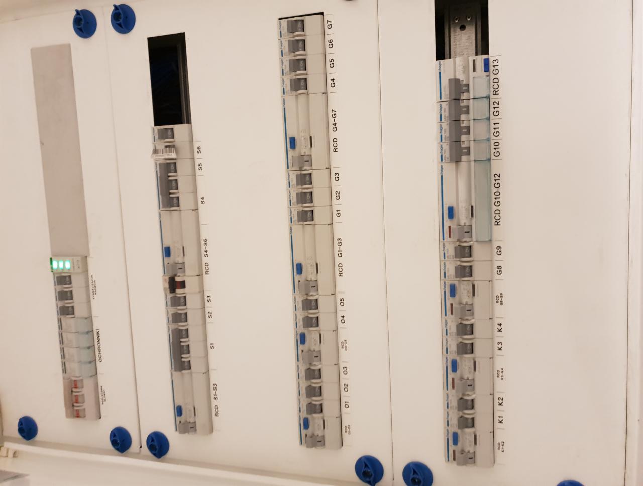 Tablica rozdzielcza z zamontowanymi bezpiecznikami i wyłącznikami różnicowoprądowymi, widoczne oznaczenia sekcji i numeracja.