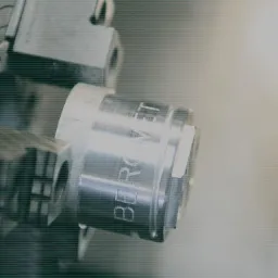 Metalowy element z wygrawerowanym napisem 'BERGVIT' mocowany w uchwycie tokarki podczas procesu obróbki.