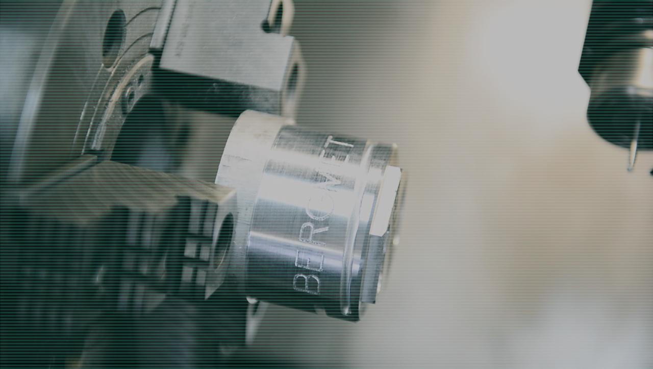 Metalowy element z wygrawerowanym napisem 'BERGVIT' mocowany w uchwycie tokarki podczas procesu obróbki.