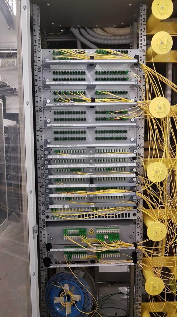 Szczegółowe ujęcie szafy telekomunikacyjnej z panelami krosowniczymi, licznymi światłowodami o żółtej barwie i elementami montażowymi, ukazujące uporządkowaną infrastrukturę sieciową.