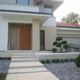 Nowoczesny dom z jasną elewacją, drewnianymi elementami i minimalistycznym ogrodem z kamieniami oraz niskimi krzewami.