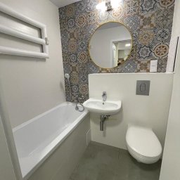 Erwin- remonty - Nowoczesna łazienka z wanną, umywalką i toaletą, wykończona płytkami w marokański wzór na ścianie za okrągłym lustrem.