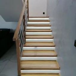 Drewniane schody z podświetleniem LED, balustrada ze stali nierdzewnej, ściana wykończona dekoracyjnym tynkiem.