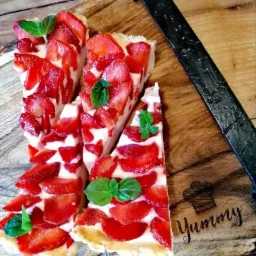 Trzy apetyczne kawałki tarty truskawkowej z kremem, udekorowane listkami mięty, ułożone na drewnianej desce z napisem 'Yummy' i metalowym uchwytem.