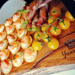 Deska z przekąskami: krakersy z łososiem i koperkiem, szparagi owinięte szynką parmeńską oraz gałązka żółtych pomidorków koktajlowych, deska z napisem Yummy.