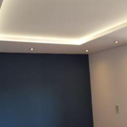 Usługi remontowe - Pokój po remoncie z granatową ścianą, białym sufitem podwieszanym z oświetleniem LED i otwartym oknem z drewnianą ramą.