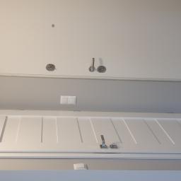 Usługi remontowe - Dwa białe, nowoczesne drzwi wewnętrzne z srebrnymi klamkami i zamkami, umieszczone w szarym pomieszczeniu. Górne drzwi gładkie, dolne z frezowanymi pionowymi liniami.