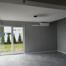 Usługi remontowe - Wnętrze pokoju po malowaniu ścian na szaro, z widokiem na ogród przez przeszklone drzwi przesuwne i nowoczesną lampą sufitową.