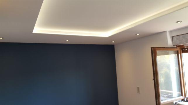 Pokój po remoncie z granatową ścianą, białym sufitem podwieszanym z oświetleniem LED i otwartym oknem z drewnianą ramą.