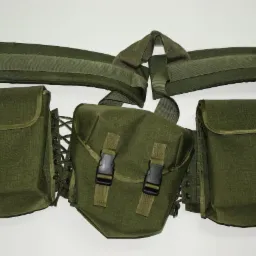 Zielona, taktyczna kamizelka modułowa z kieszeniami i pasami mocującymi, widoczna na białym tle. Wykonana z trwałego materiału.