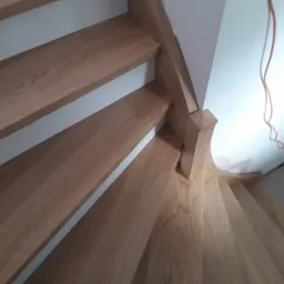 Drewniane schody z jasnego drewna w trakcie montażu, widoczne niedoskonałości wykończenia i narzędzia pracy na podłodze.