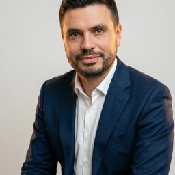 Kancelaria Adwokacka Adwokat Michał Tropper - Portret mężczyzny w ciemnej marynarce i jasnej koszuli, z lekkim zarostem, na jasnym tle. Profesjonalny wizerunek, idealny jako zdjęcie profilowe adwokata.