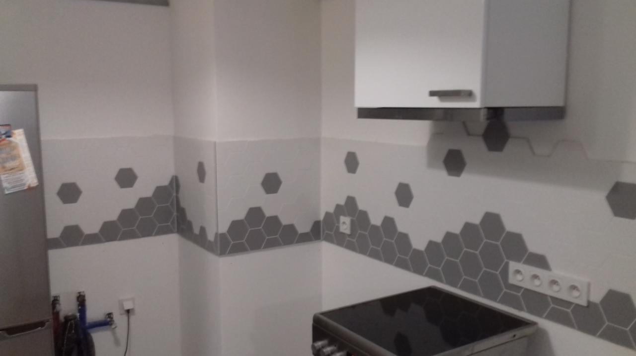 Wykończona kuchnia z szarymi heksagonalnymi płytkami na ścianie, białe szafki wiszące i widoczna płyta grzewcza.