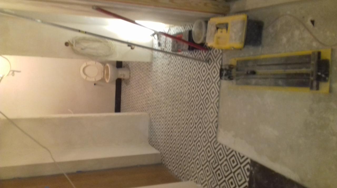 Remont łazienki w trakcie: położone płytki z geometrycznym wzorem, widoczny sedes, narzędzia do cięcia płytek i wiadro.