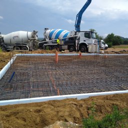 BARTZ Bartłomiej Wylężek - Zbrojenie fundamentu w szalunku ze styropianu, widoczne dwie betoniarki i pracownicy w tle.