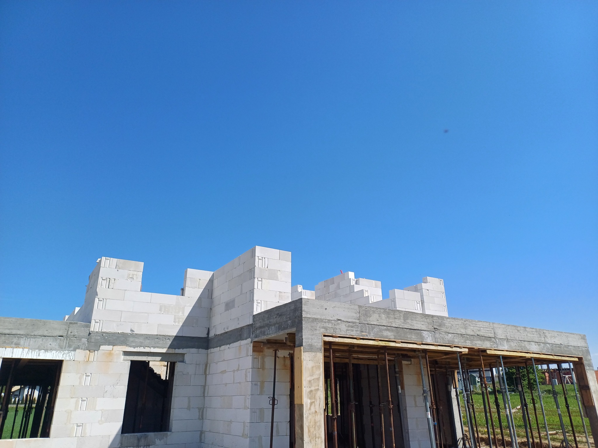 Surowy stan domu z betonu komórkowego w trakcie budowy, widoczne szalunki i podpory stropu, na tle błękitnego nieba.