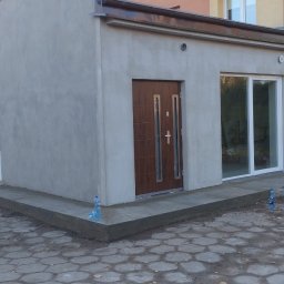 Piotr P - Budynek po szpachlowaniu i malowaniu elewacji zewnętrznej, widoczna nowa stolarka okienna i drzwiowa, teren wokół budynku częściowo zagospodarowany.