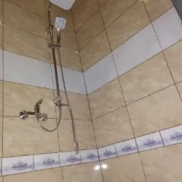 Wykończona kabina prysznicowa z beżowymi płytkami, dekoracyjnym pasem z motywem wody i nowoczesną armaturą z deszczownicą i słuchawką.