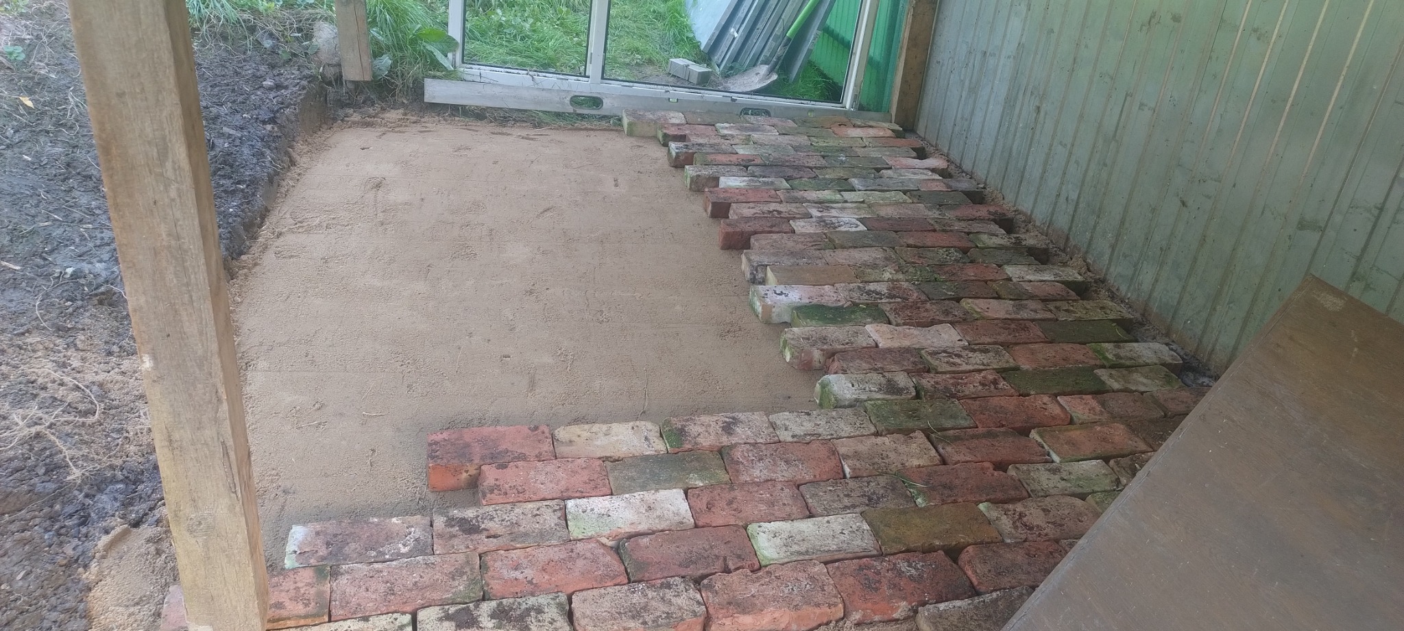 Układanie ceglanej podłogi wewnątrz budynku, widoczny fragment piaskowego podłoża i poziomica przy oknie.