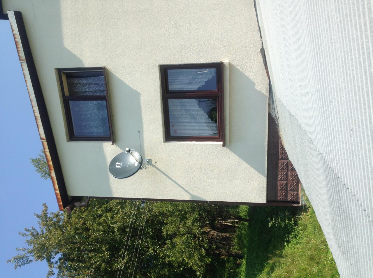 Antena satelitarna zamontowana na elewacji budynku w Żywcu, widoczna z poziomu ogrodu, z fragmentem okna i dachu.
