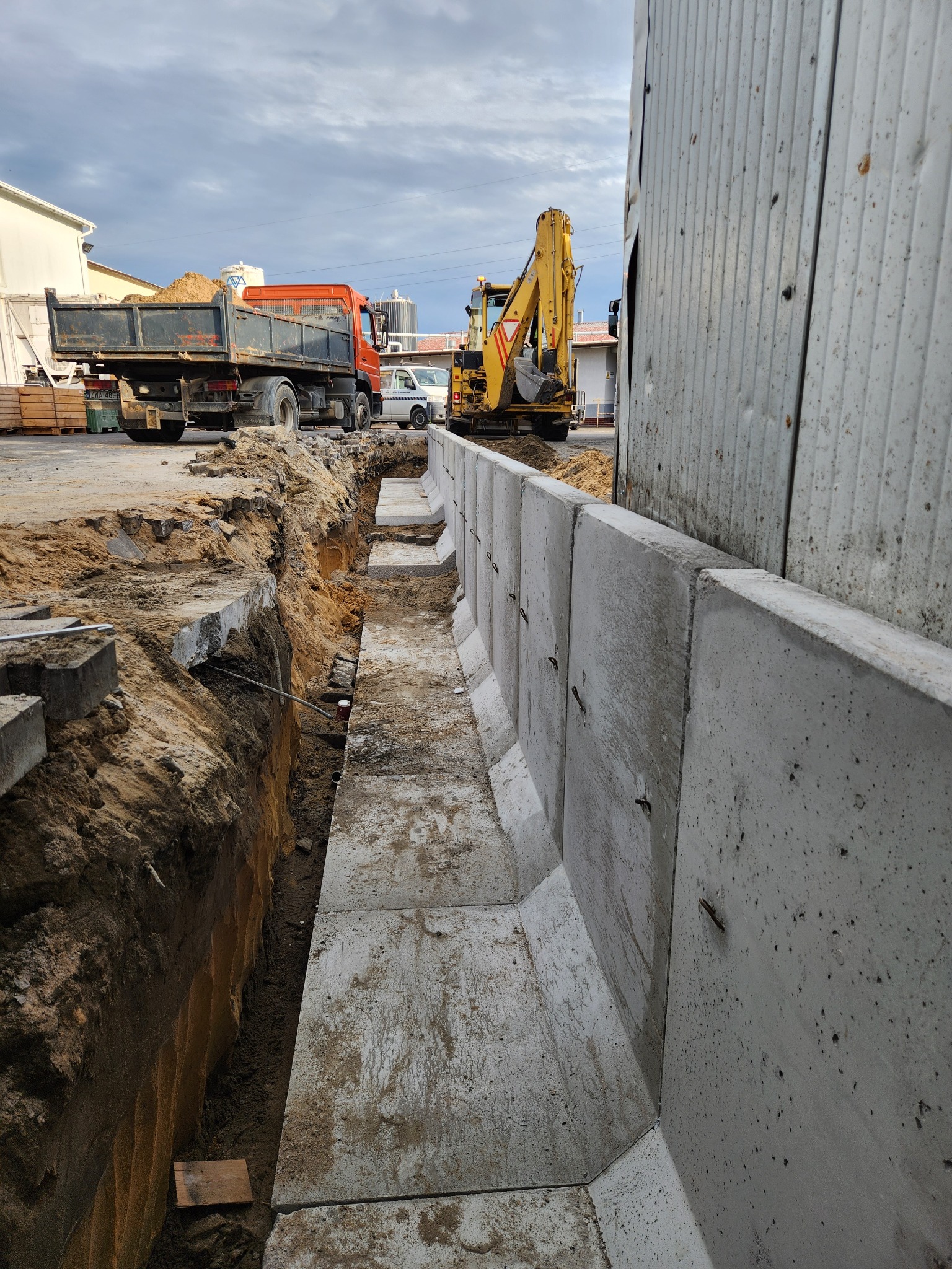 Wykop z prefabrykatami betonowymi, koparka i wywrotka w tle. Widoczne zbrojenia w prefabrykatach. Realizacja robót ziemnych i budowlanych.