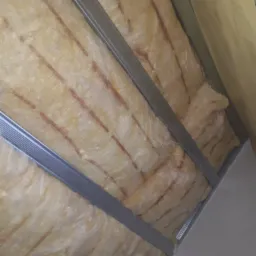 Izolacja z wełny mineralnej pomiędzy metalowymi profilami w konstrukcji poddasza, widok z dołu.