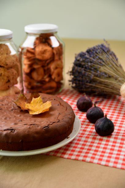 Czekoladowe ciasto na talerzu z jesiennym liściem, figi, suszone jabłka w słoiku i bukiet lawendy na czerwono-białym obrusie w kratkę.