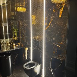 Ładny Dom - Elegancka, czarna łazienka z marmurowymi płytkami, podświetleniem LED, wiszącą toaletą i pisuar, oświetlona ozdobnym żyrandolem.