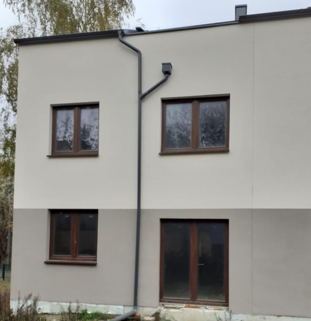 Dwukondygnacyjny budynek z oknami w brązowych ramach i szarym systemem rynnowym, elewacja w dwóch odcieniach beżu, widok z zewnątrz.