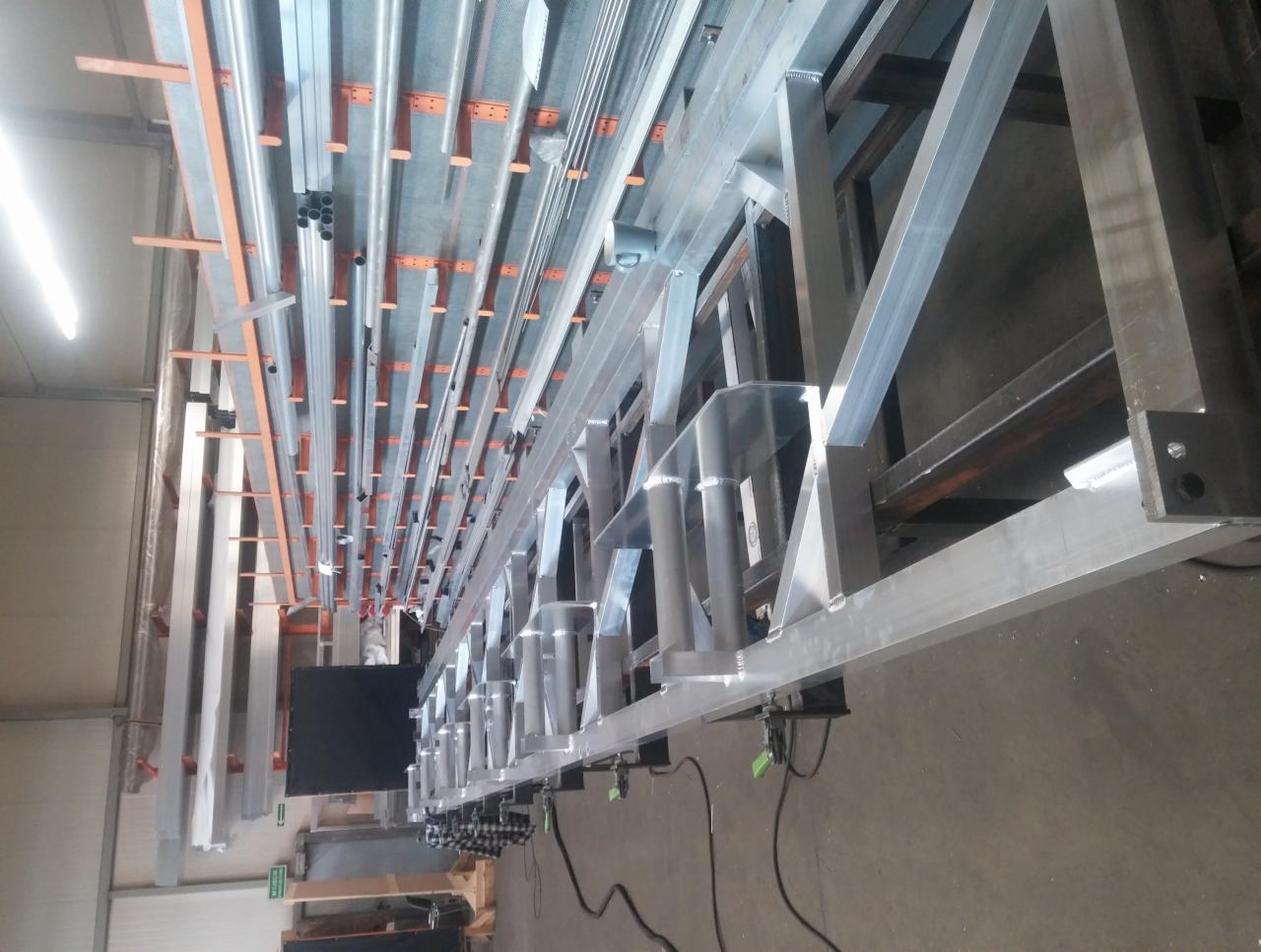 Konstrukcja stalowa ze spawanych profili aluminiowych w hali produkcyjnej, widoczne spawy i elementy mocujące, z perspektywy dolnej.