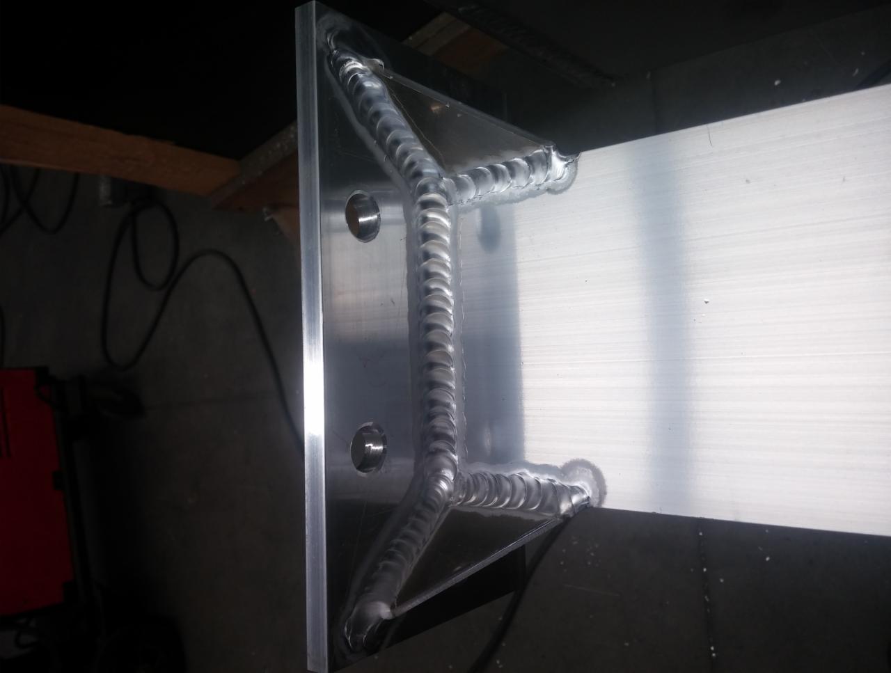 Spoina aluminium w kształcie litery Y na płaskowniku z otworami, widoczne ślady obróbki powierzchniowej.