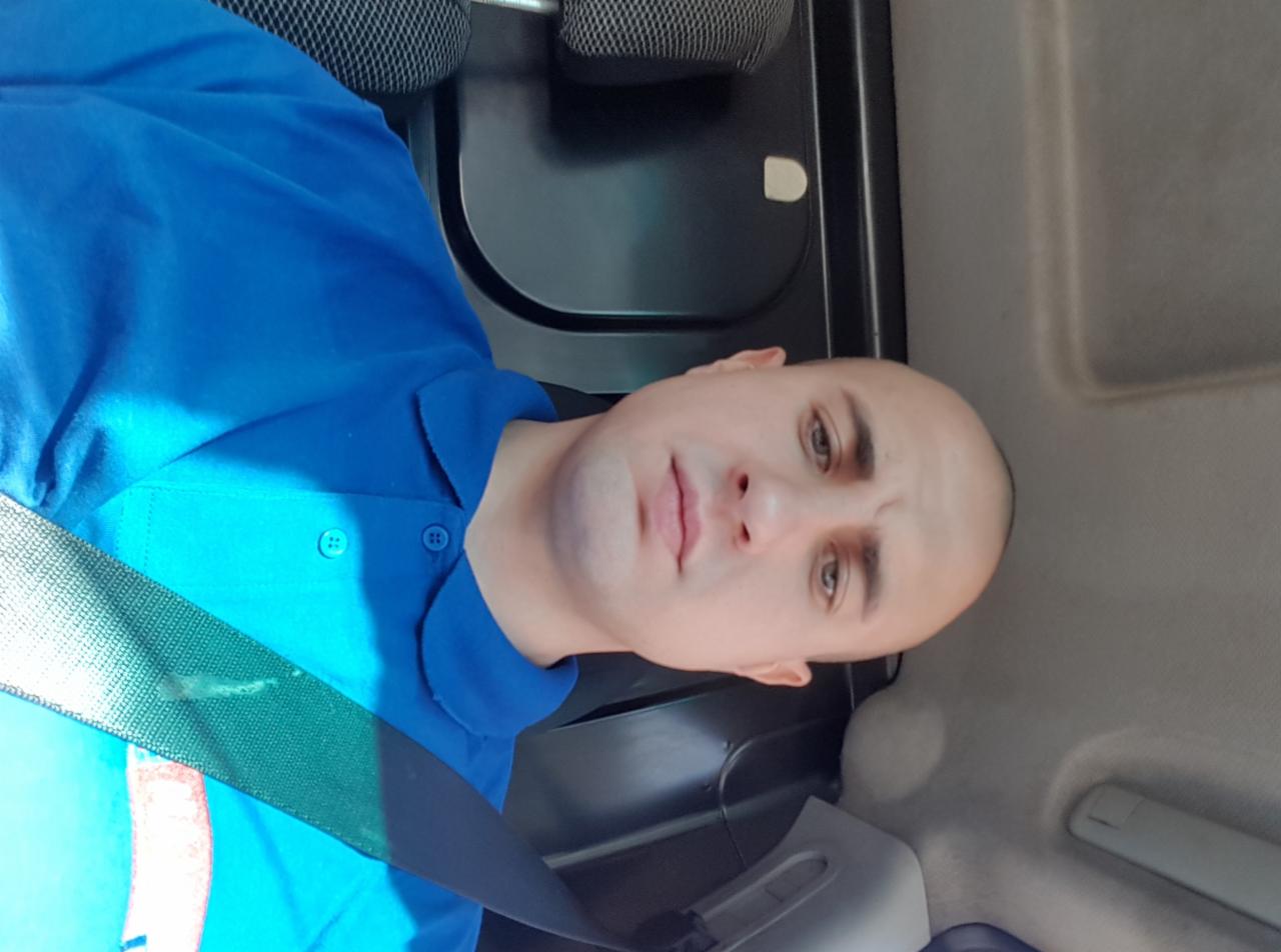 Autoportret mężczyzny w niebieskiej koszuli, siedzącego w samochodzie z zapiętym pasem bezpieczeństwa. Ujęcie z góry, widoczna część wnętrza pojazdu.