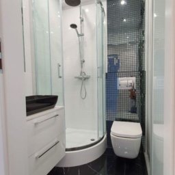 Salbox - Nowoczesna łazienka z czarną marmurową podłogą, kabiną prysznicową narożną z przezroczystego szkła, białą umywalką nablatową i toaletą w zabudowie na tle ściany wyłożonej mozaiką.