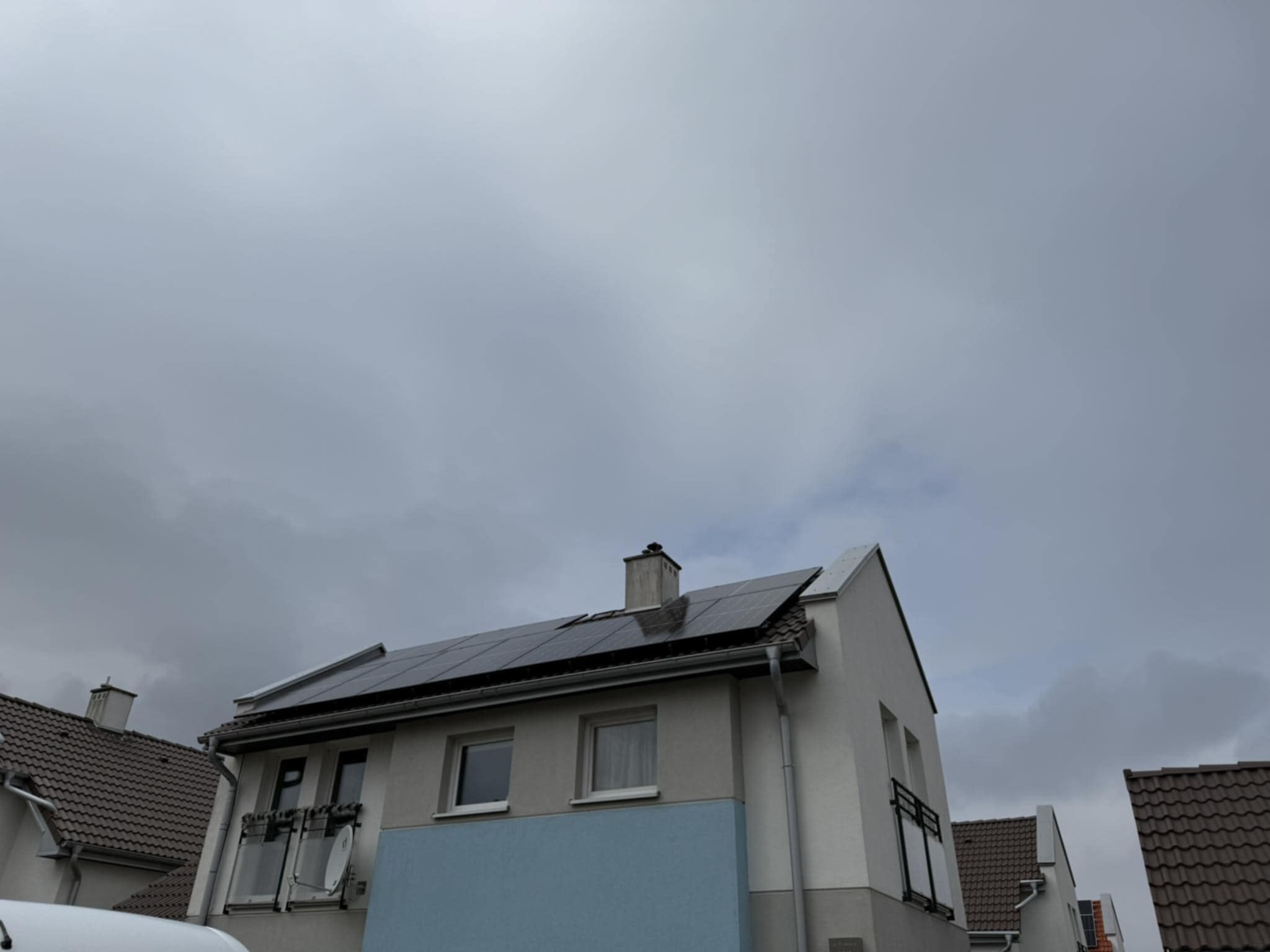 Dom jednorodzinny z panelami słonecznymi na dachu, widok z dołu na tle pochmurnego nieba. Instalacja paneli fotowoltaicznych na skośnym dachu.