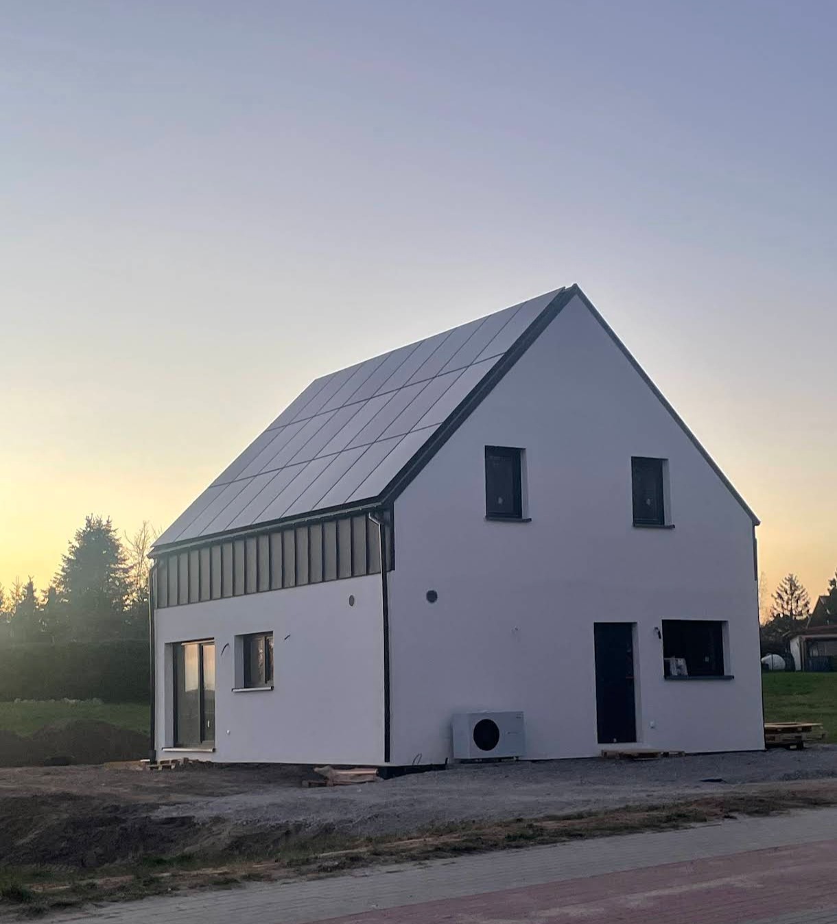 Biały dom jednorodzinny z panelami słonecznymi na dachu, widok z zewnątrz o zmierzchu. Zamontowana klimatyzacja na elewacji.