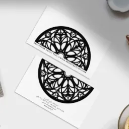 Dwie wizytówki pracowni architektonicznej Katarzyna Zając z graficznym motywem półokrągłego okna witrażowego w kolorze czarnym, leżące na białym biurku obok kawy, ołówka i metalowej miarki.