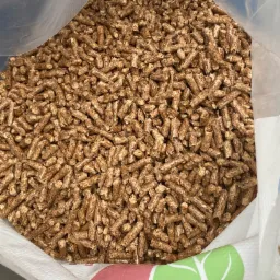 Worek wypełniony po brzegi brązowymi, drobnymi granulkami pelletu, widoczny fragment etykiety z zielonym motywem liścia.